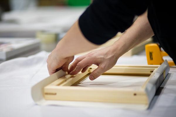 Person stretching canvas over wooden frame for art print preparation.