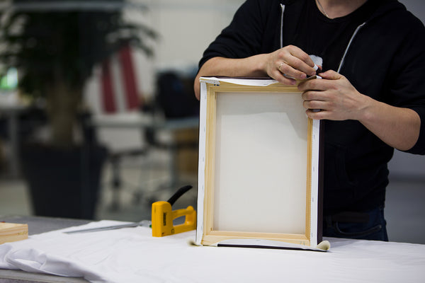 Person hand-stretching canvas print over solid wood stretcher bars