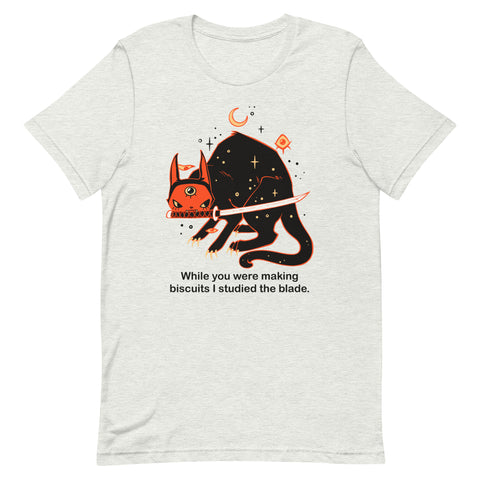 Orion the black cat graphic tee with text 'While you were making biscuits I studied the blade' in vibrant colors.