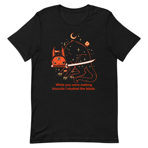 Orion the black cat graphic t-shirt featuring the quote, 'While you were making biscuits I studied the blade' in vibrant orange.