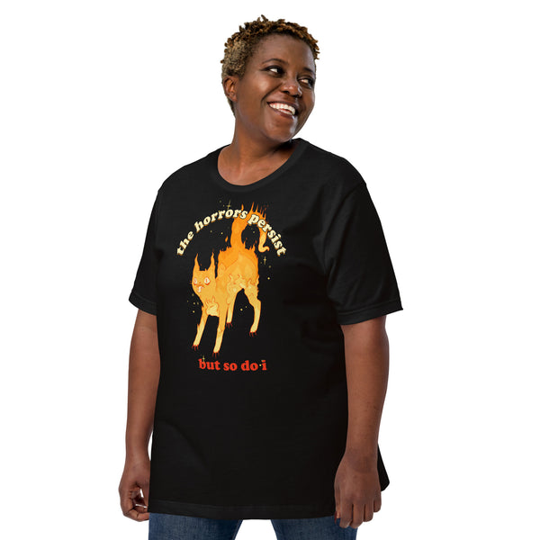 Person wearing a black unisex T-shirt with a fire cat illustration and the quote "The horrors persist but so do I." Perfect for goth and witchy fashion lovers.