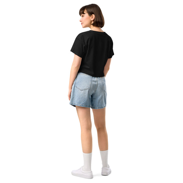 Woman in black crop top and denim shorts facing backward, showcasing relaxed fit and dropped shoulders. Casual summer outfit style.