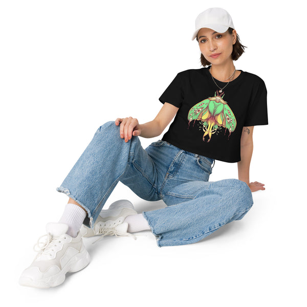 Woman wearing black relaxed crop top with hand-drawn green luna moth design, paired with blue jeans and white sneakers.